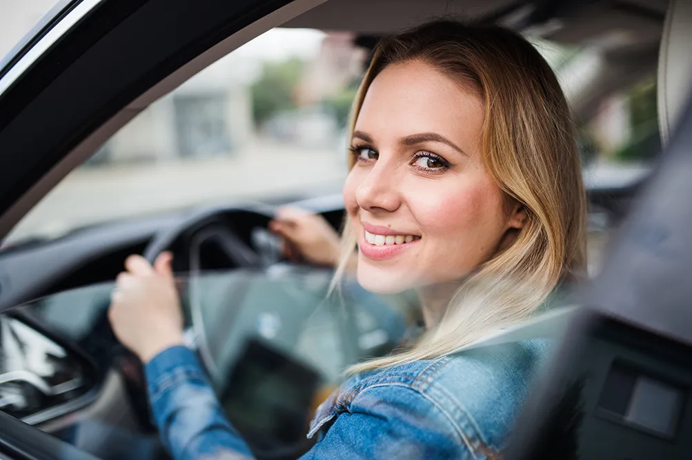 Junge Fahrerin sitzt im Auto und schaut hinaus.